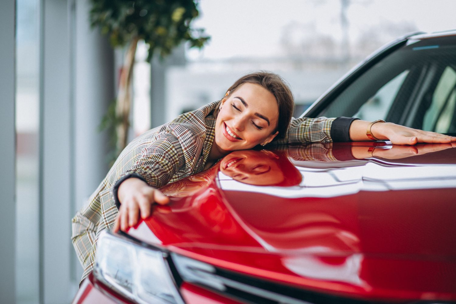 Frau umarmt lächelnd die Motorhaube eines roten Autos im Showroom.